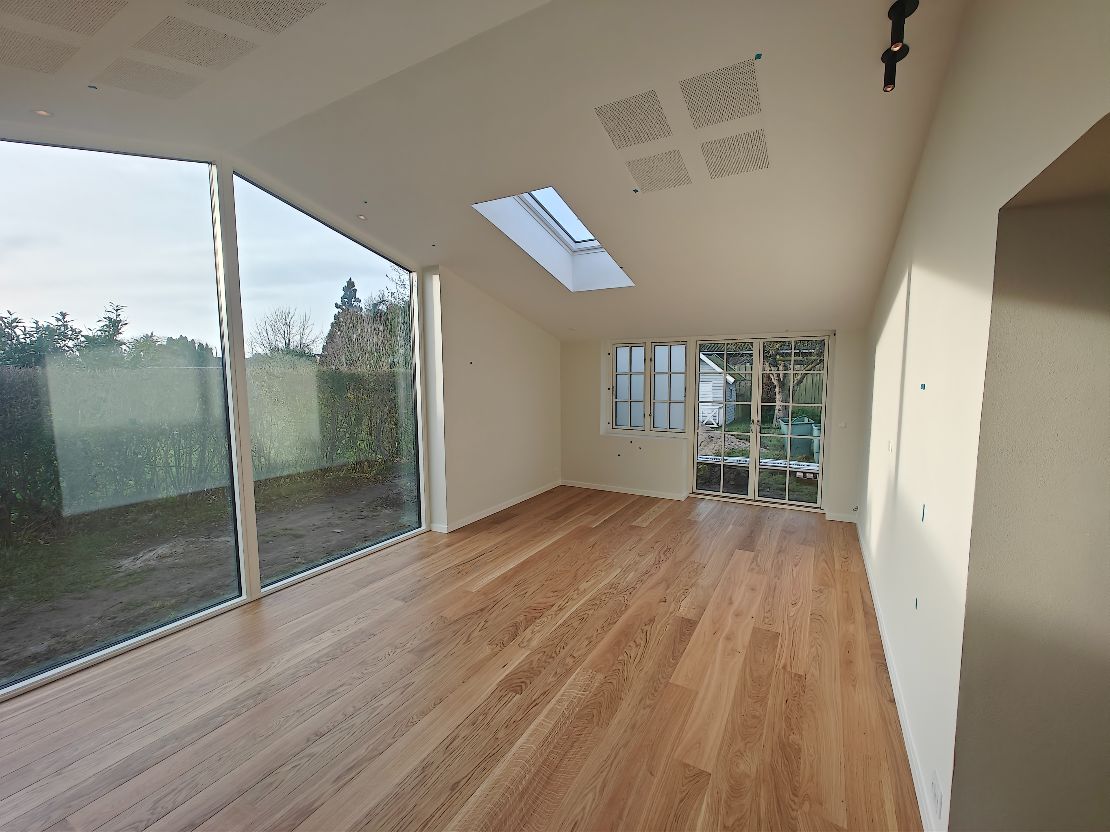 Lyst og rummeligt værelse med store vinduer, skråtag og lyst trægulv.