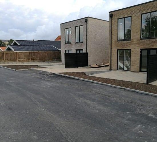 Nye moderne huse med store vinduer og indkørsel på en asfalteret vej i et boligområde.