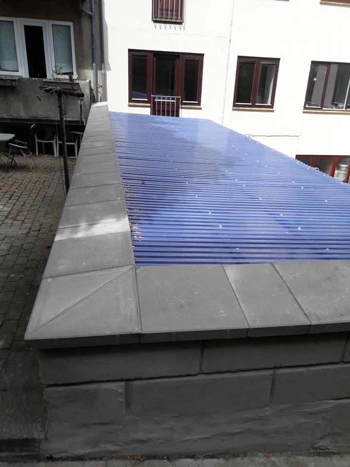 Flad tagterrasse med blå tagplader og grå betonkanter i en bymiljø.