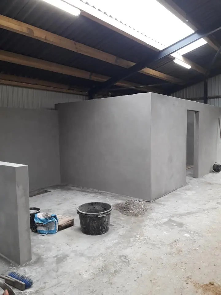 Byggeri af vægge i en garage med grå cement, spande og værktøj synligt på gulvet.