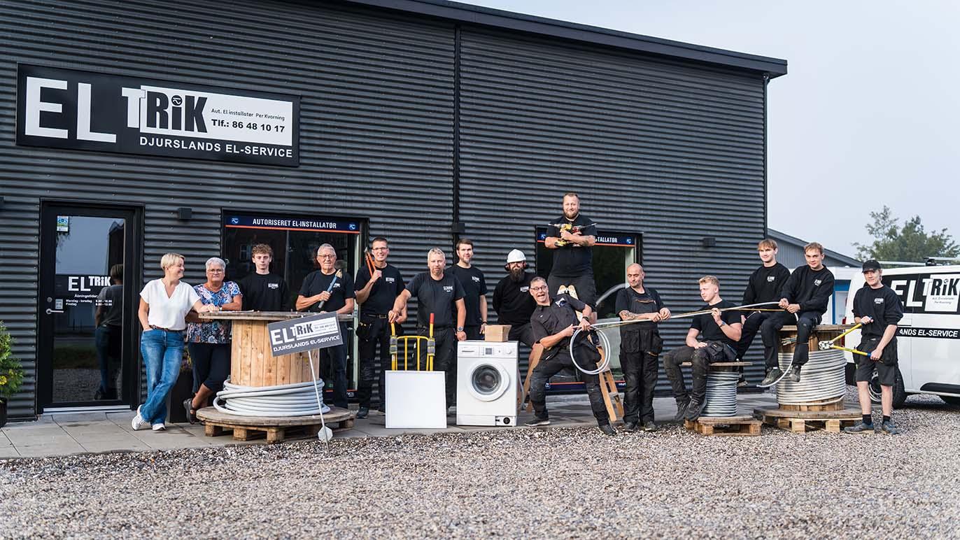 Gruppe af medarbejdere fra ELTRIK står foran bygningen med elektriske apparater og kabler.