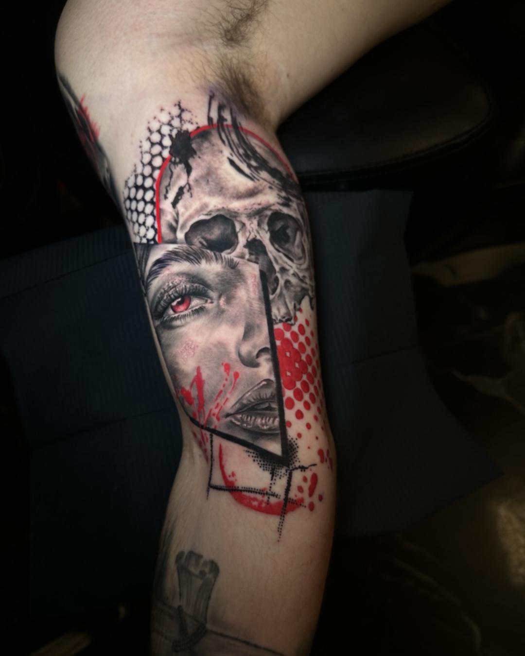 Farverig tatovering på en arm med et ansigt og et kranium, prydet med røde og sorte detaljer.