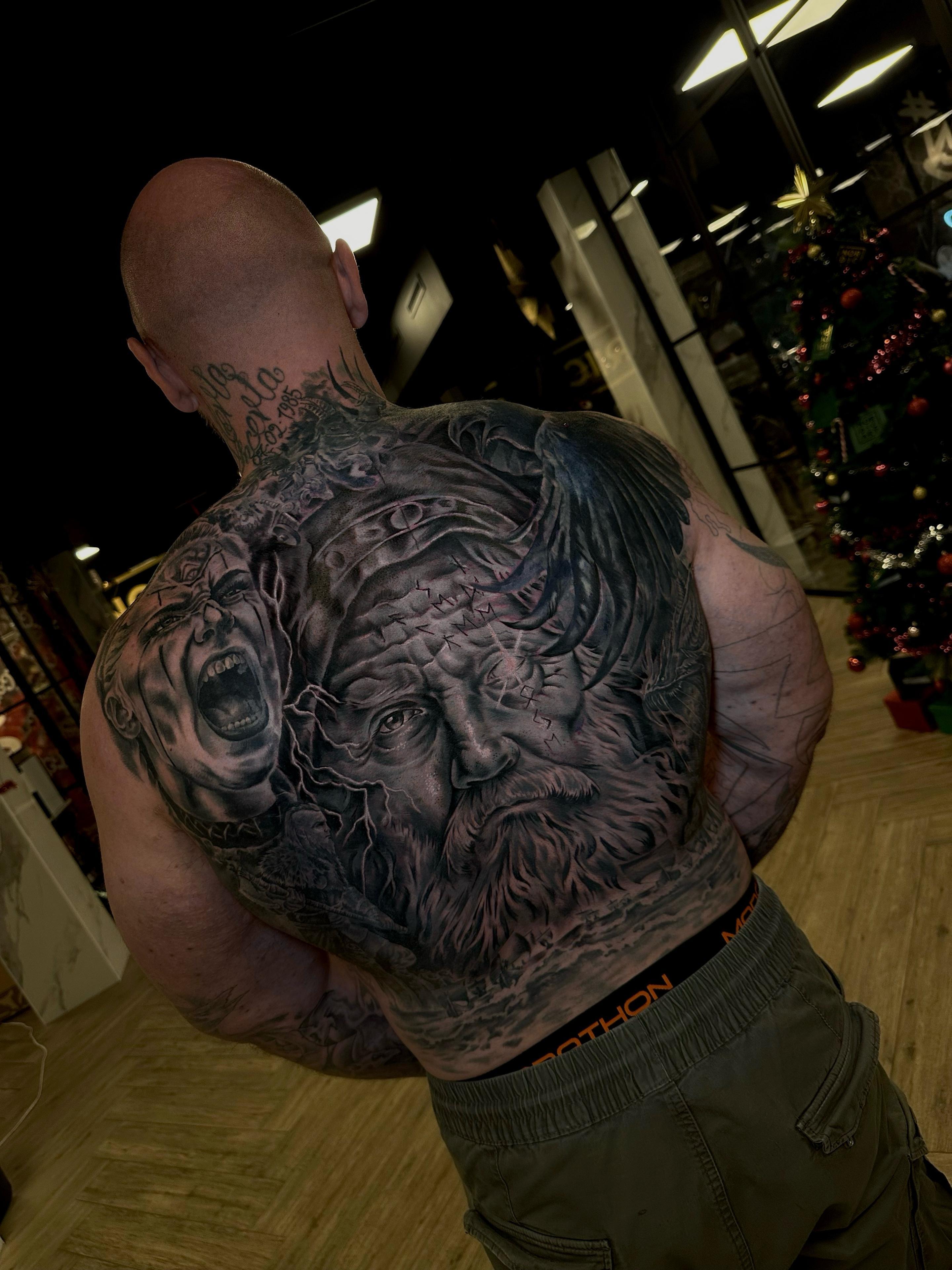 Mand med detaljeret rygtattoo, der viser ansigtet af en gammel mand og forskellige symboler.