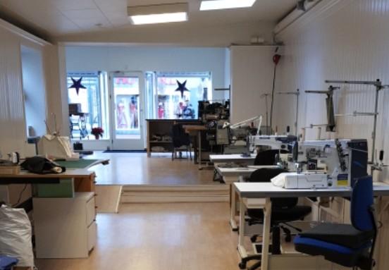 Syværksted med symaskiner, borde og stole, beliggende i en lys og rummelig butik.
