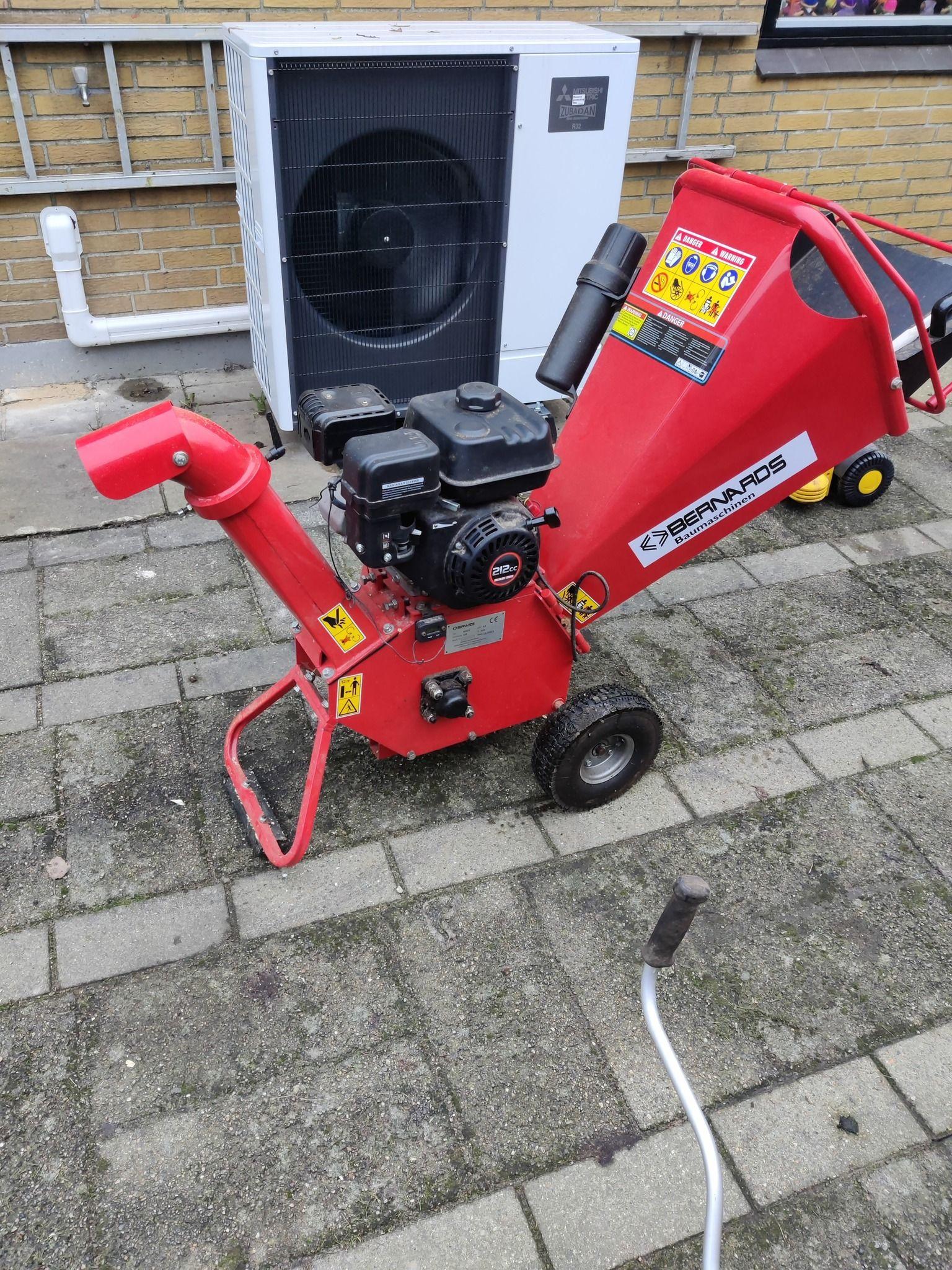 Rød haveaffaldshakker med motor, placeret på fliser i en have.