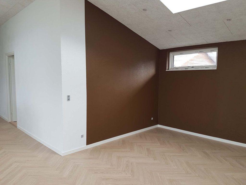 Lys stue med hvid væg og en brun væg, skrå loft og vindue, der giver naturligt lys.