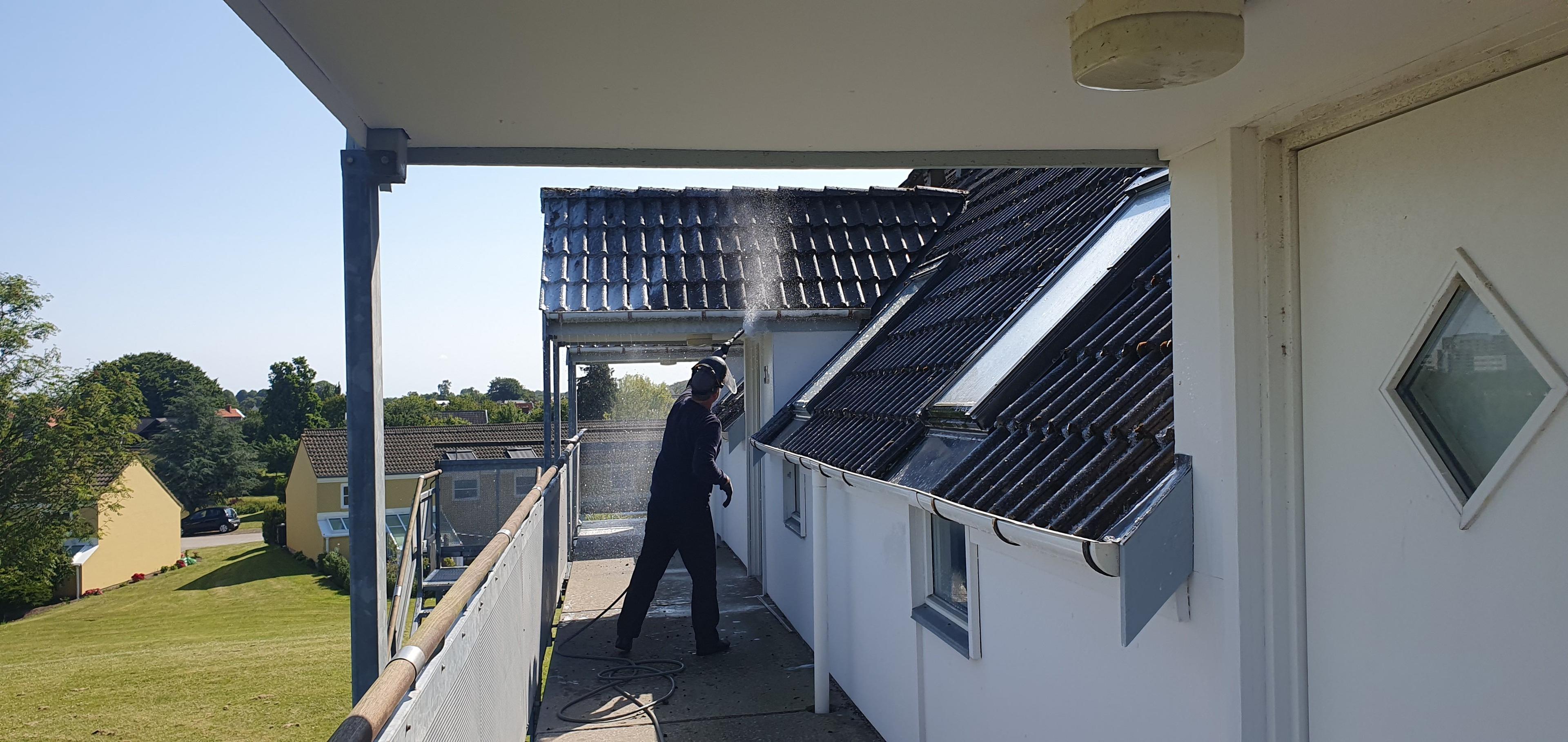 En mand står på en balkon og renser taget med en højtryksrenser på en solrig dag.