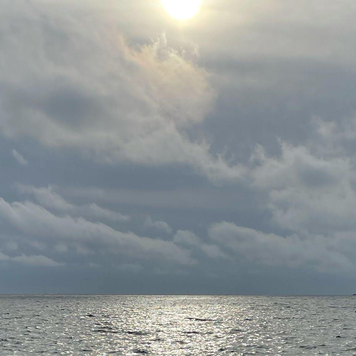 Solskin skinner over havet med mørke skyer i baggrunden og en glitrende vandoverflade.