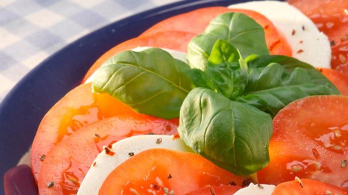 Frisk salat med skiver af tomat, mozzarella og basilikum på en blå tallerken.