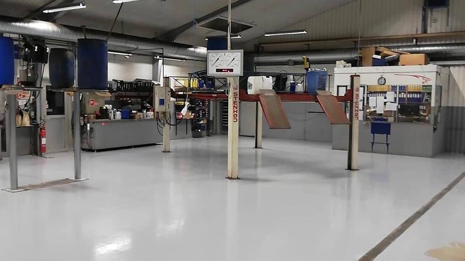 Et værksted med flere arbejdsstationer, værktøj og en ren, lys gulvbelægning.