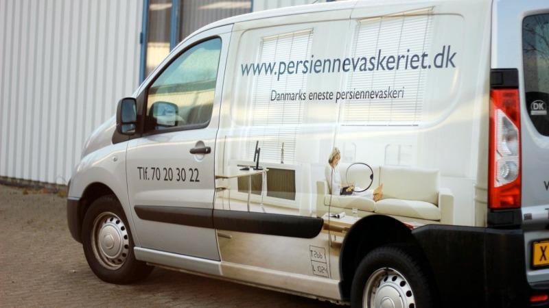 En varevogn med reklame for persiennevaskeri, der viser en lys stue og kontaktinformation.