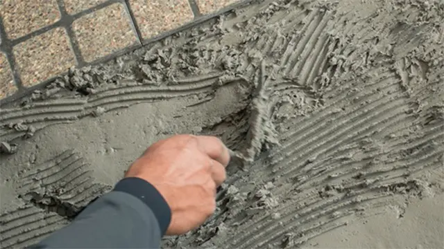 Hånd, der arbejder med cement, og skaber mønstre på en nylagt overflade.