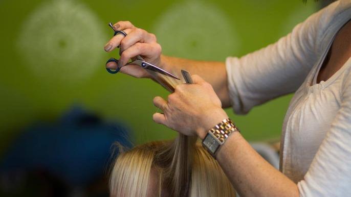 En frisør klipper hår på en kunde i en farverig salon med grønne vægge.
