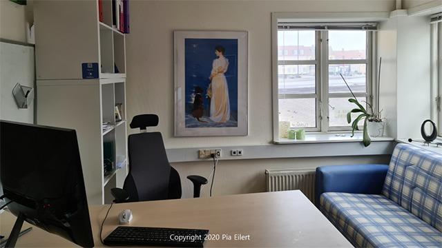 Et kontor med en computer, en stol, en sofa og et maleri af en kvinde ved vinduet.
