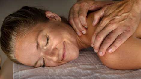 Kvinde får massage med afslappet ansigtsudtryk, mens hænder masserer hendes ryg på en massagebriks.