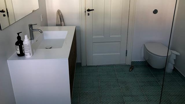 Moderne badeværelse med hvid vask, træskab, spejl og grønne fliser på gulvet.
