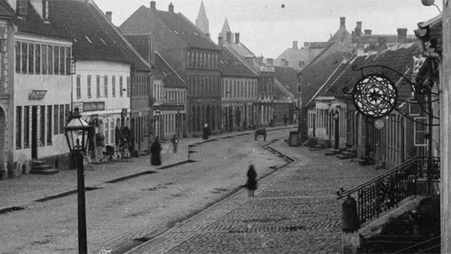 En stille gade med gamle bygninger, brosten og lamper, der skaber en nostalgisk atmosfære.