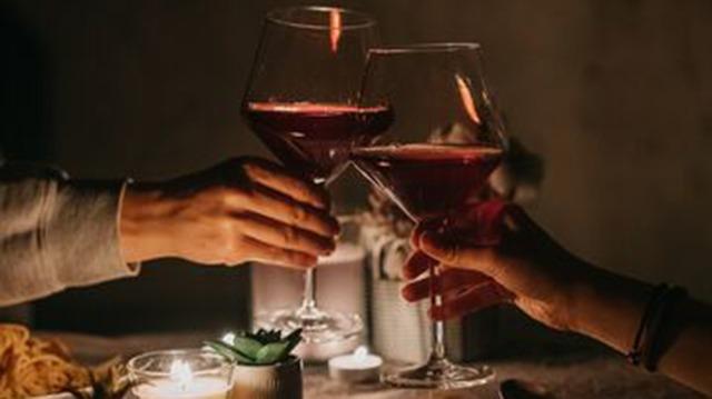 Toasting with red wine in elegant glasses at a romantic dinner table with candles and soft lighting.