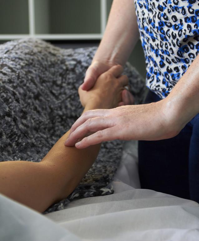 En person holder en andens hånd, mens de ligger på en seng med en blød dyne.