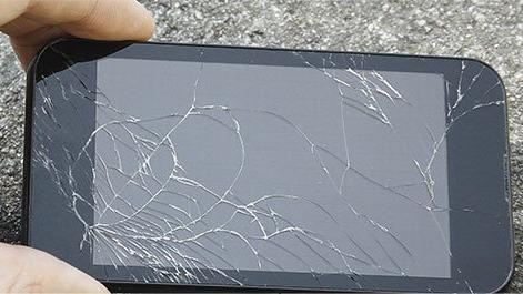 En hånd holder en smartphone med en revnet skærm, der viser tydelige sprækker og skader.