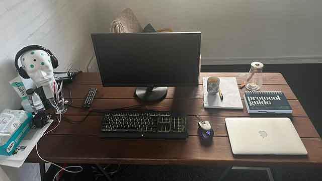Et skrivebord med en computer, tastatur, mus, notesbog, vandflaske og en robotfigur.