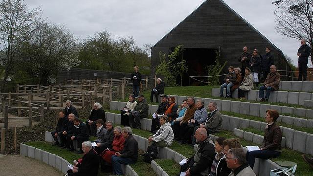 En gruppe mennesker sidder på en trappe i et udendørs amfiteater med en bygning i baggrunden.