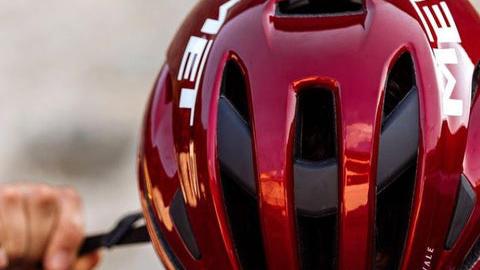 Rød cykelhjelm med sorte detaljer, der bliver justeret af en person.