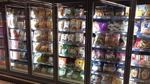 Fryser med forskellige fødevarer, herunder snacks, grøntsager og færdigretter, oplyst af LED-lys.