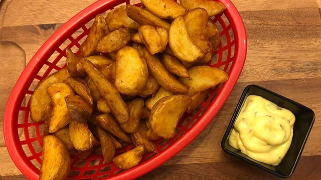 Sprøde kartoffelbåde i en rød kurv med en skål mayonnaise ved siden af.