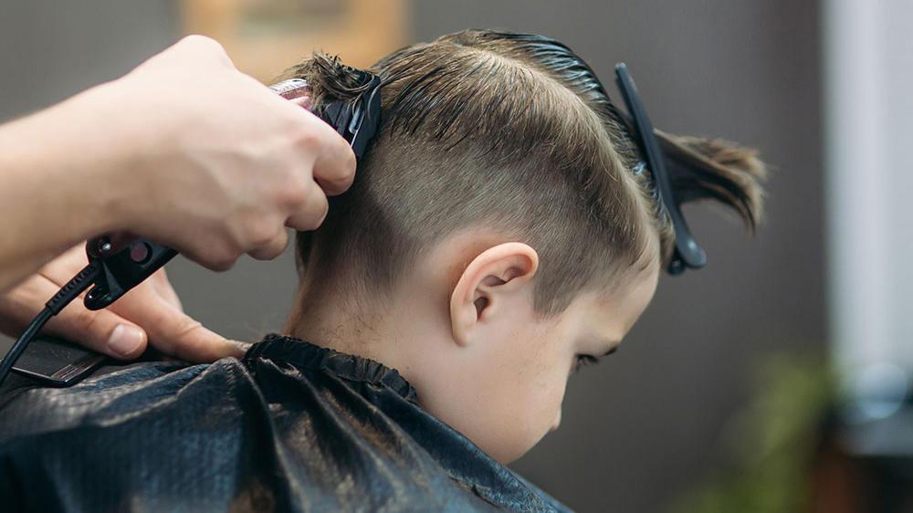 En frisør klipper håret på en dreng, der sidder i en sort kappe i en frisørsalon.