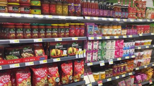 Hylder i en supermarked fyldt med forskellige fødevarer, herunder saucer, snacks og te.