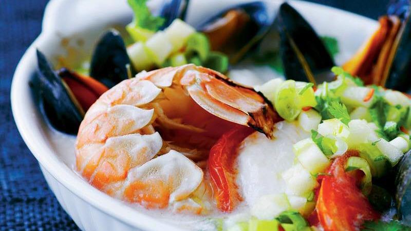 En skål med rejer, muslinger og grøntsager i en cremet suppe.