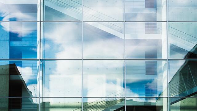 Refleksioner af skyer i et moderne glasbyggeri med geometriske former og strukturer.