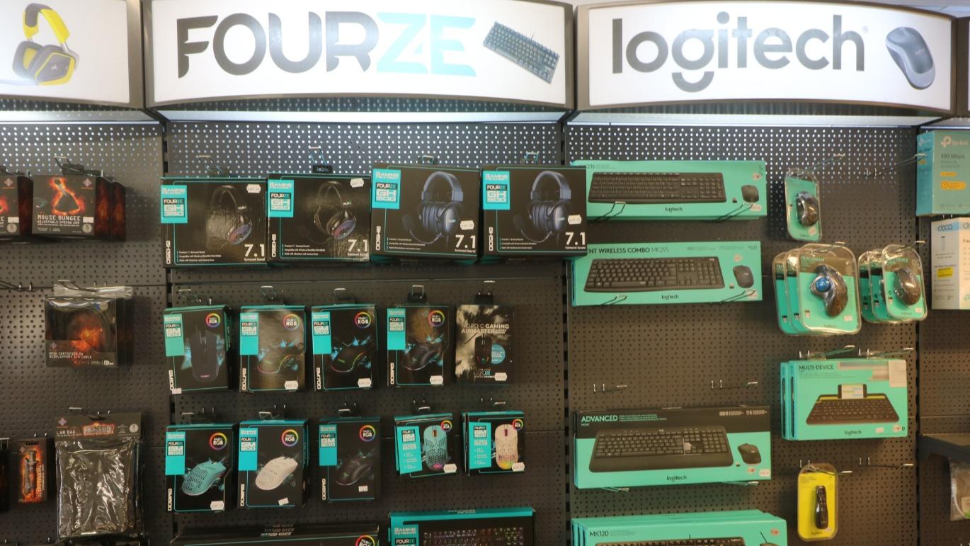 Hylder med computertilbehør fra FOURZE og Logitech, herunder mus, tastaturer og hovedtelefoner.