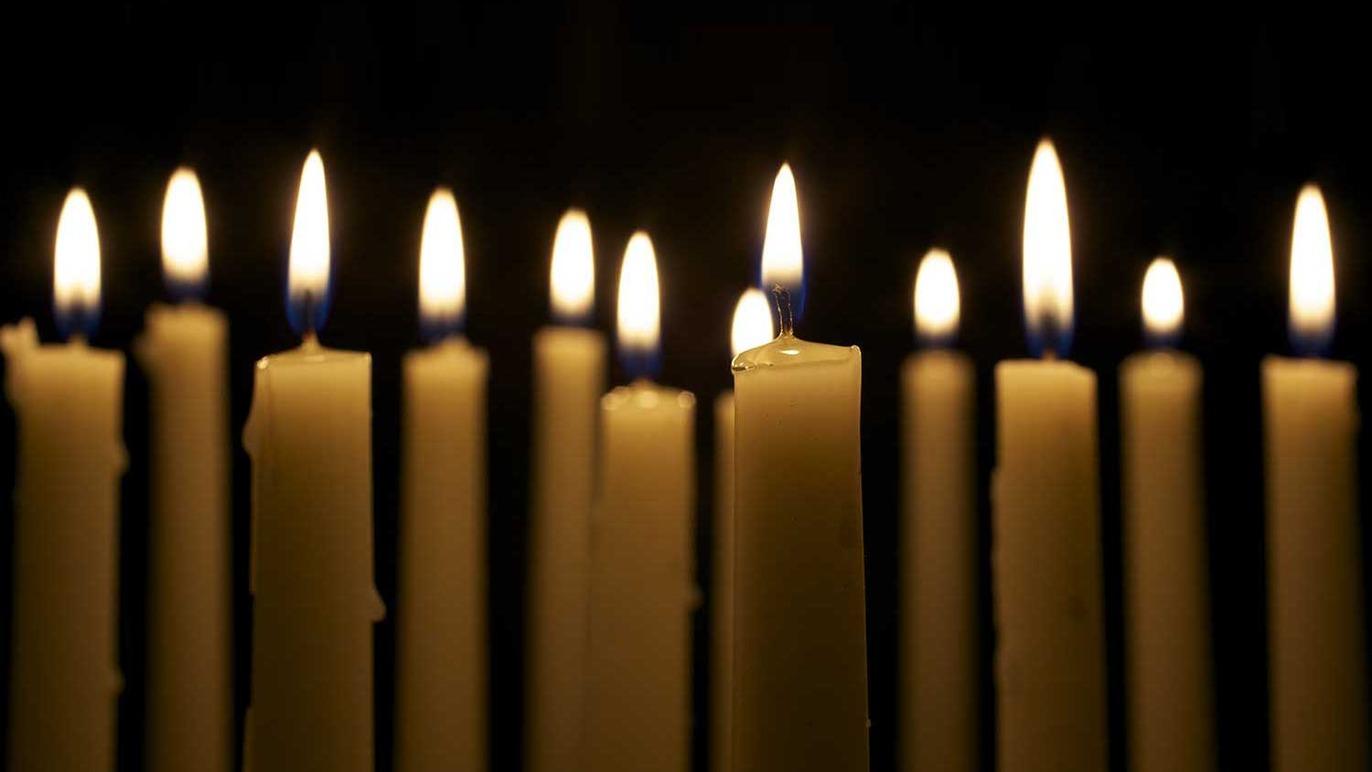 En række tændte stearinlys med flammer, der lyser op i mørket.