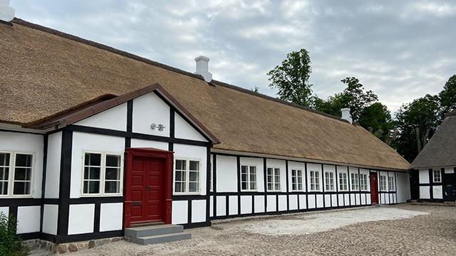 Et traditionelt dansk hus med stråtag og hvidt bindingsværk, beliggende i en landskabelig setting.