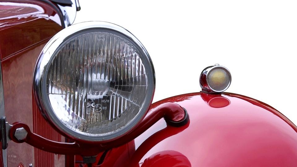 Nærbillede af en rød bils forlygter med kromdetaljer og en ekstra lygte på motorhjelmen.