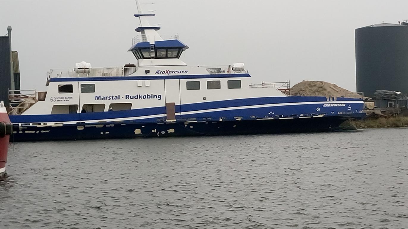 Færgen "Marius" ligger ved kajen med en blå og hvid farve, omgivet af vand og industrielle bygninger.