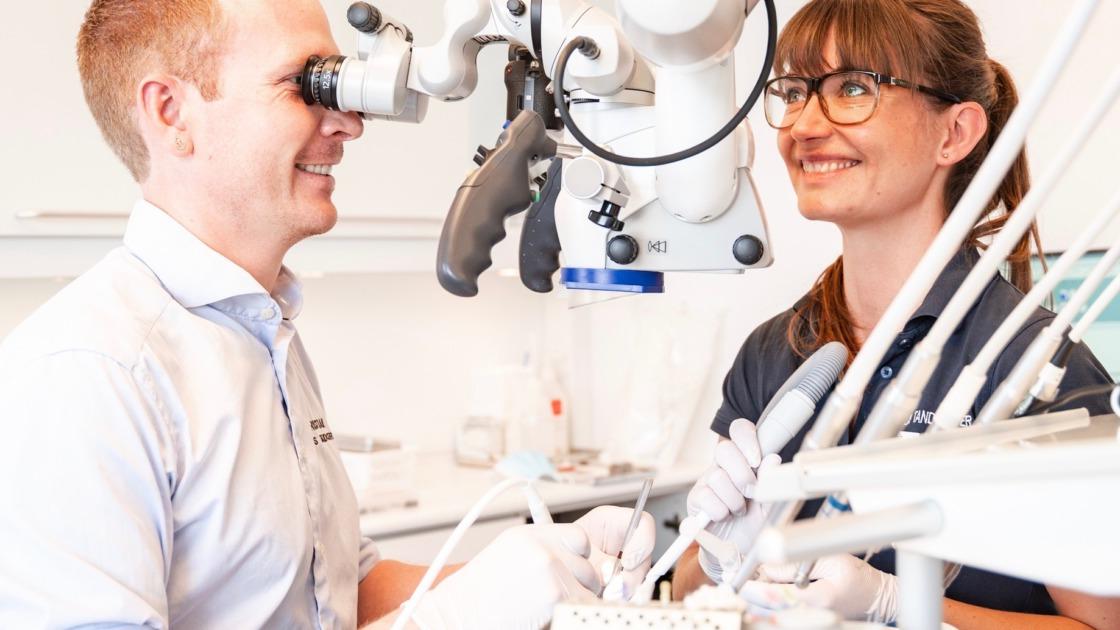 En tandlæge og en assistent arbejder sammen med et mikroskop i en moderne tandklinik.