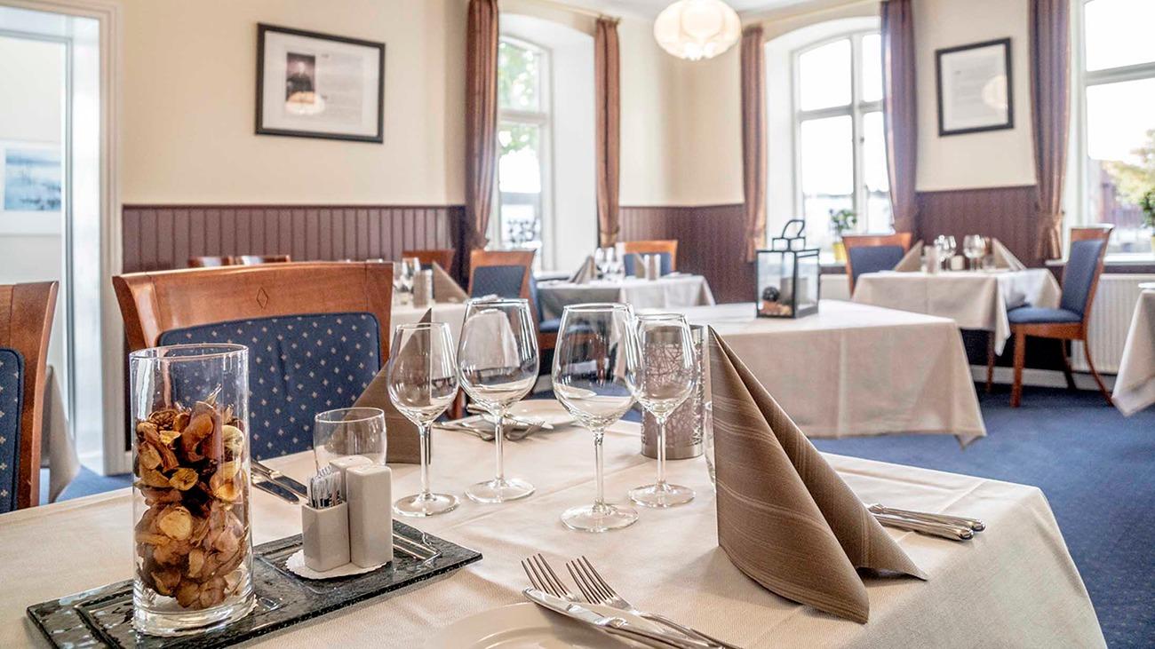 Elegant restaurantindretning med dækkede borde, glas og servietter i en lys og indbydende atmosfære.