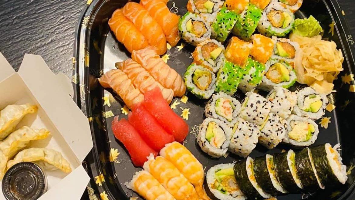 En sushi-tallerken med forskellige typer sushi, herunder laks, tun, og grøntsager, samt dumplings ved siden af.