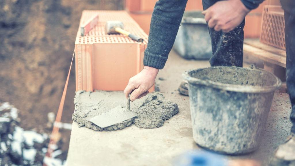 Håndværker arbejder med cement på en byggeplads, mens han bruger en spade og en spand.