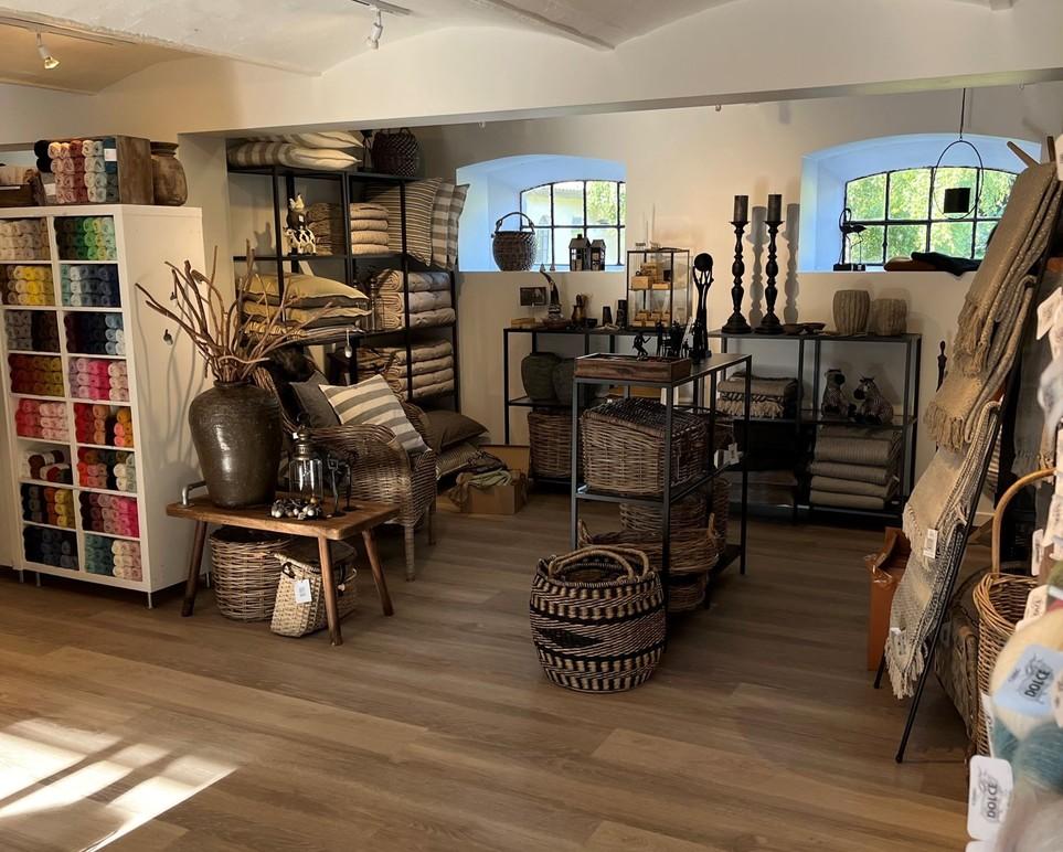 En hyggelig indretning af en butik med kurve, tekstiler og farverige hylder fyldt med garn og boligtilbehør.