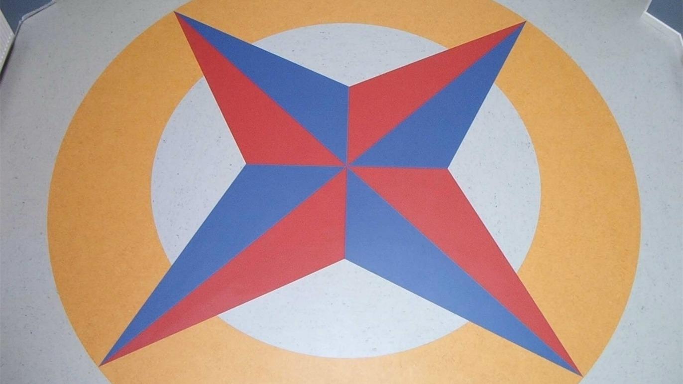 Farverig geometrisk stjerne med røde, blå og orange sektioner på en lys baggrund.