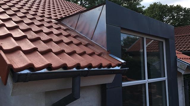 Tag med røde teglsten og moderne vinduesparti på et hus.
