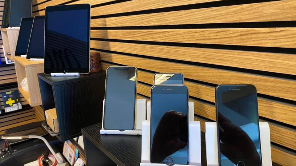 Flere smartphones og en tablet præsenteret på hylder i en elektronikbutik.
