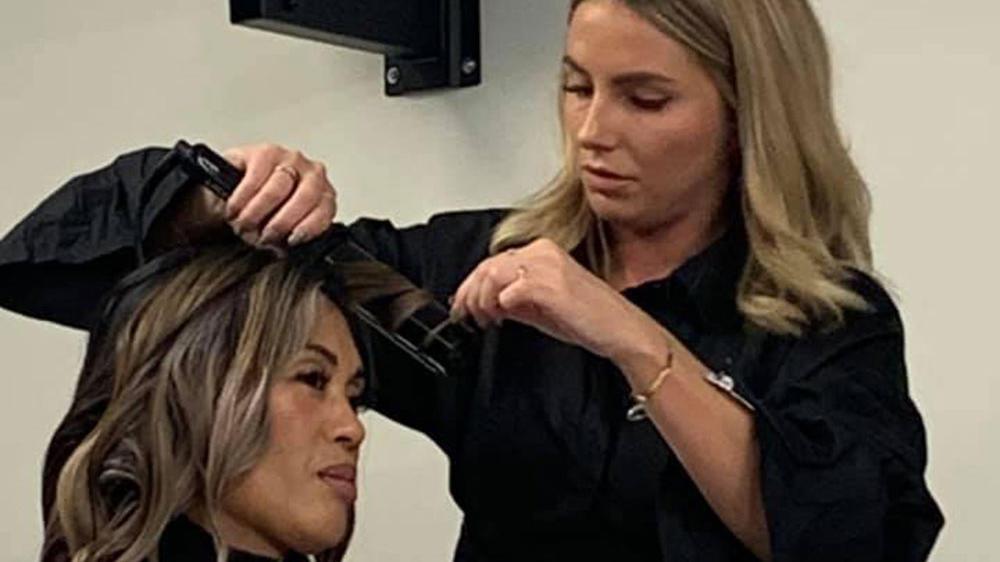 En frisør styler hår på en kunde med en krøllejern i en moderne salon.