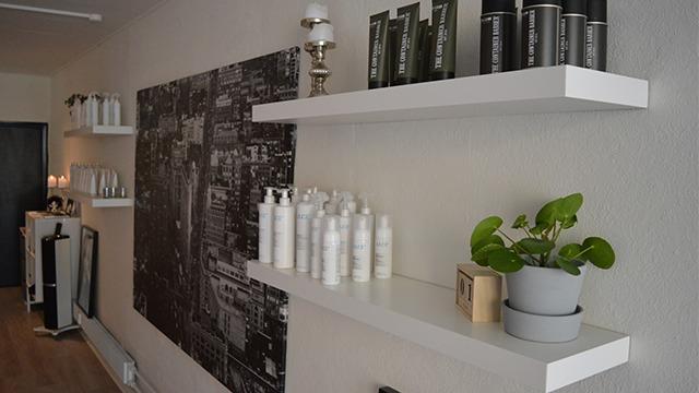 Hylder med skønhedsprodukter og en plante i en moderne salon med en stor vægkunst af en by.