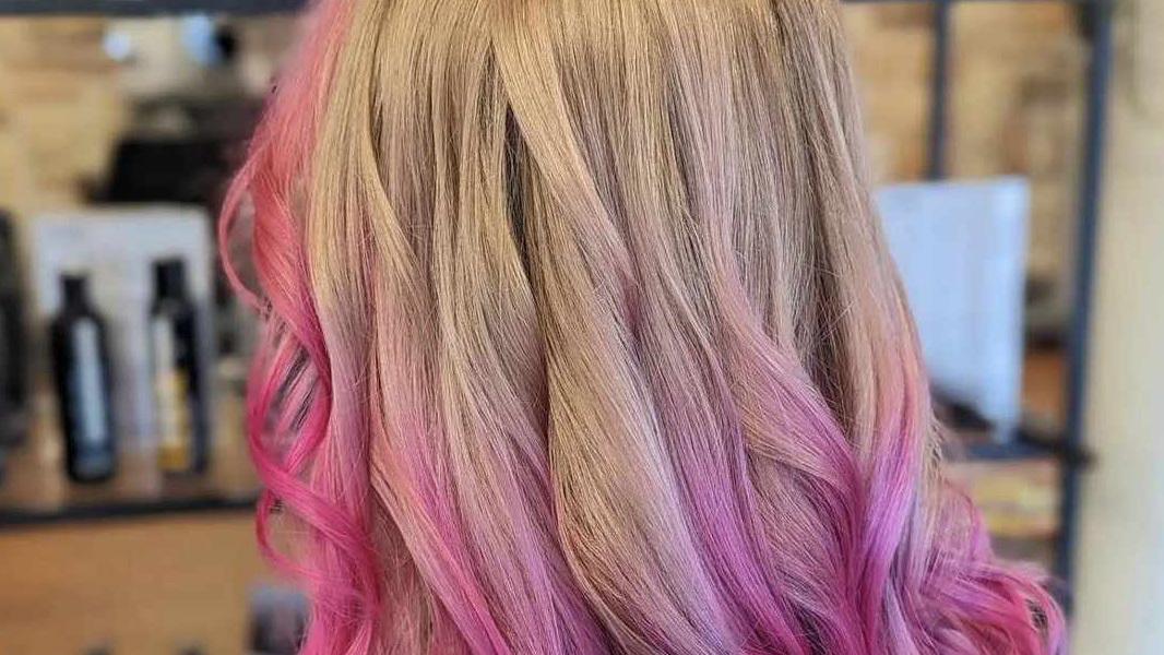 Hår med en gradient fra blond til lyserød, bølger og glansfulde stråler i en frisørsalon.