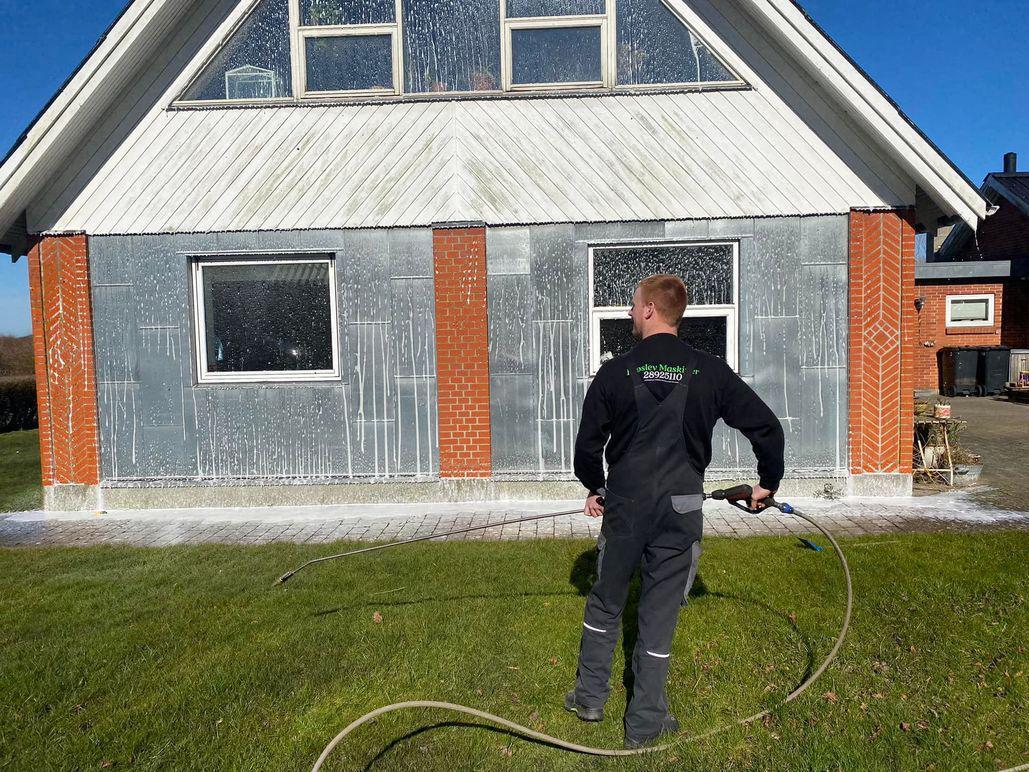 Mand der vasker en husfacade med højtryksrenser på en solrig dag.